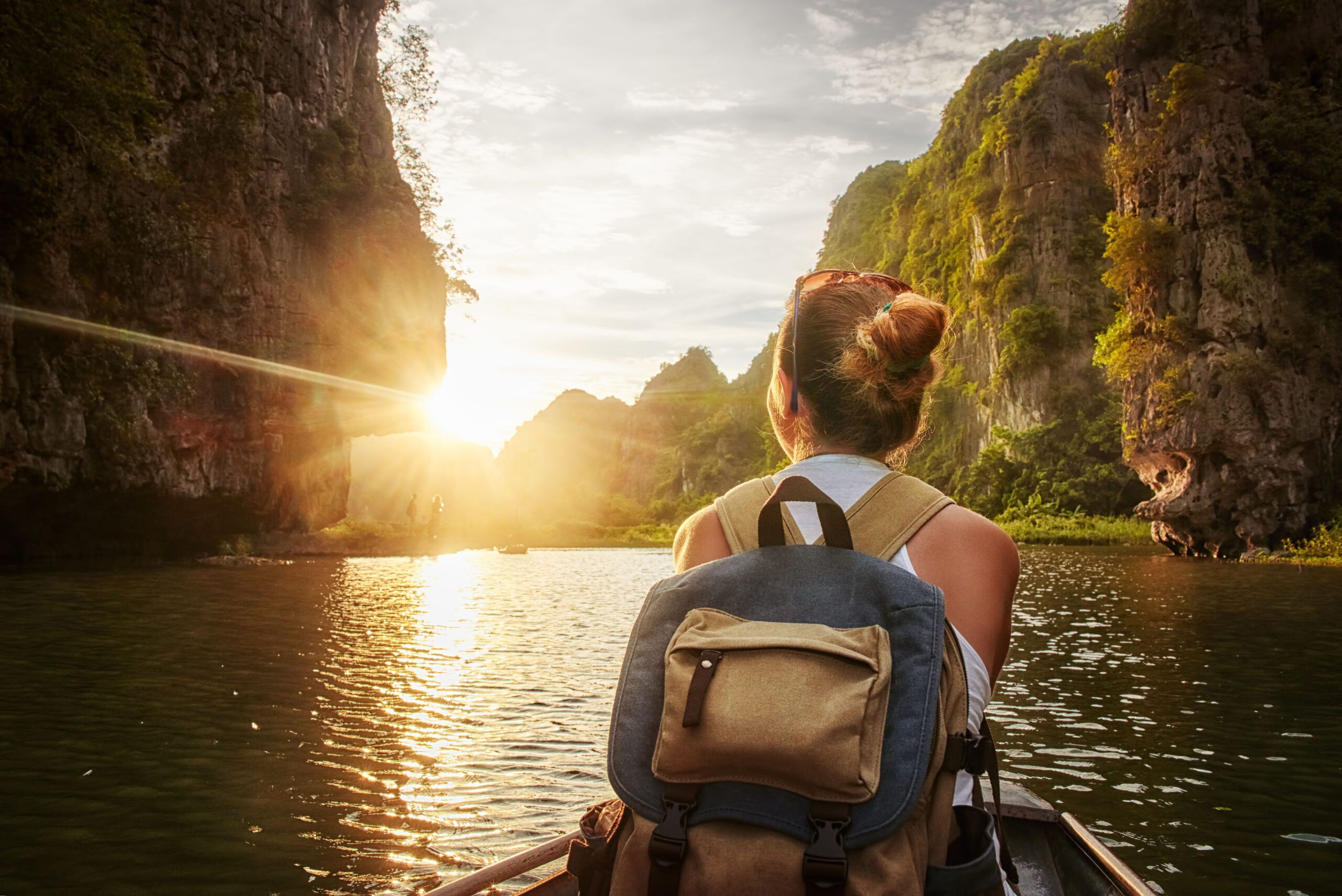 Happy woman with backpack traveling by boat enjoying sunset among of karst mountains in the North of Vietnam. Travel and active lifestyle, summer holiday concept.